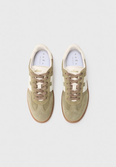 Een paar beige suède sneakers met witte zijstrepen, bruin veters en rubberen zolen, van bovenaf bekeken op een witte achtergrond.