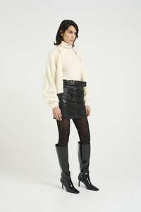 Cream knit sweater, black leather mini skirt with multiple belts, sheer black tights, and glossy knee-high black stiletto boots.