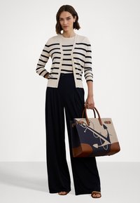 Striped cream and navy cardigan, wide black trousers, and a large canvas tote with anchor design, brown leather accents, and sturdy handles.