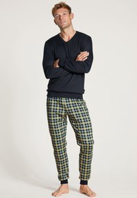 Haut à col en V à manches longues de couleur marine associé à un pantalon de pyjama à motifs pied-de-poule en vert, jaune et bleu. Les pantalons ont des chevilles côtelées.
