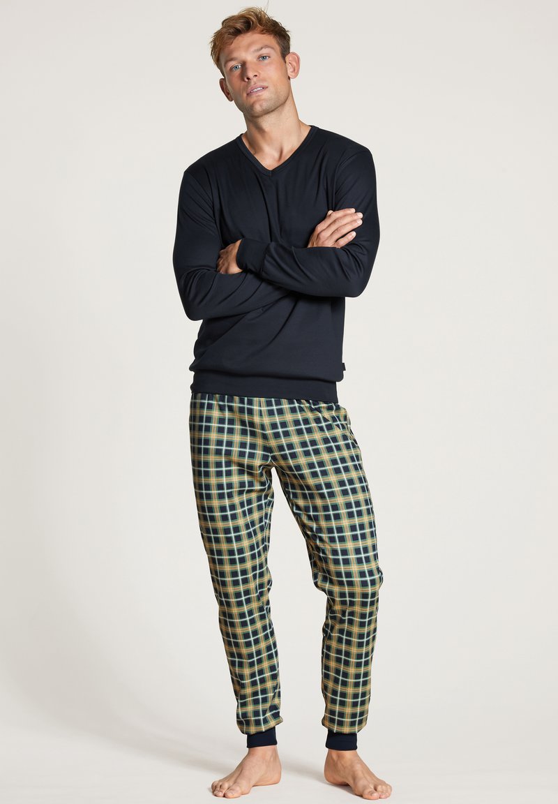 Haut à col en V à manches longues de couleur marine associé à un pantalon de pyjama à motifs pied-de-poule en vert, jaune et bleu. Les pantalons ont des chevilles côtelées.