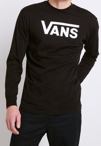 T-shirt a maniche lunghe in cotone nero con un grande logo bianco "VANS" sulla parte frontale. Design aderente con polsini a coste e scollatura a girocollo.