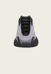 Sapatilha atlética cinza com um cabedal liso, atacadores pretos e sola de borracha. Apresenta detalhes numa tonalidade mais escura e um silhueta aerodinâmica.
