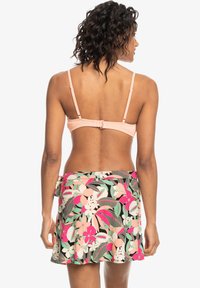 Virágmintás bikini szett, amely egy barack színű, állítható pántos toppal és egy hozzá illő, színes virágmintás szoknyával rendelkezik.