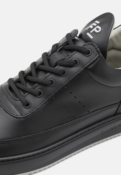 Svart lädersneaker med platta svarta snören, perforerad detaljering på sidan och en kontrasterande vit sula med märkning.