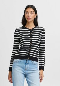 Cardigan rayé noir et blanc avec un col rond, fermeture à boutons à l'avant et manches longues. Fabriqué en matière tricotée texturée. Accents de boutons dorés.
