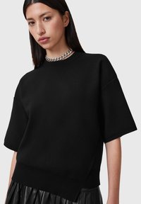 Felpa nera oversize a maniche corte con orlo a costine e spacchi laterali. Presenta una texture liscia e una vestibilità rilassata. Accento con collana a catena argentata.