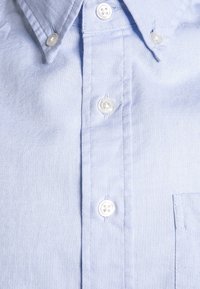 Jasnoniebieska koszula na guziki z teksturowanej tkaniny, z małą kieszonką na piersi i białymi guzikami. Kołnierzyk o wyraźnych krawędziach.