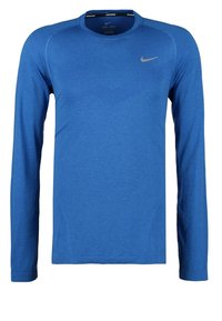 Niebieska sportowa koszulka z długim rękawem, wykonana z lekkiego materiału. Posiada okrągły dekolt i subtelne detale teksturalne. Logo Nike w kolorze srebrnym.