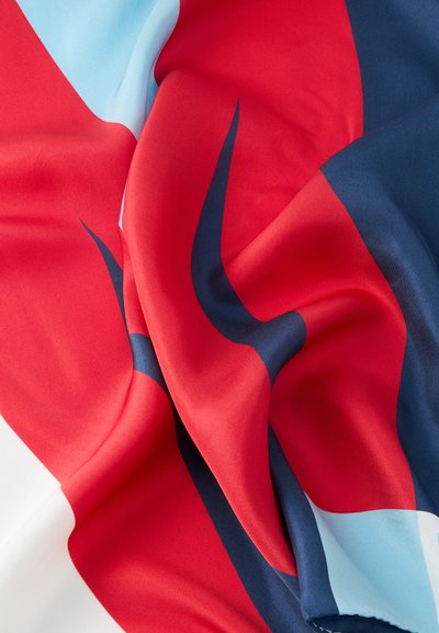 Sileä kangas, jossa rohkea geometrinen kuvio punaisena, tummansinisenä, vaaleansinisenä ja valkoisena, esitetty luonnollisilla laskoksilla ja pehmeällä tekstuurilla.