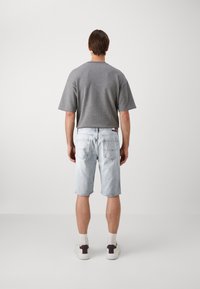 Grå kortermet avslappet t-skjorte sammen med lyseblå denimshorts. Antrekket er komplettert med hvite sko med mørke hælaksenter.