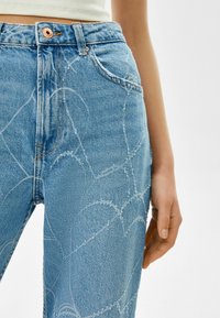 Ljusblå denimjeans med hög midja, med ett diskret vitt hjärt-mönster, kopparknapp och sydda detaljer.