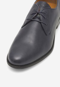Granatowe skórzane buty o gładkiej fakturze, z wąskim noskiem i okrągłymi sznurówkami. Charakteryzują się subtelnym gołym szwem oraz trwałą podeszwą.