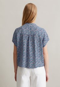 Korte mouw met bloemenpatroon in lichte stof. Blauwe achtergrond met roze en groene accenten, met een geplooid ontwerp aan de achterkant.