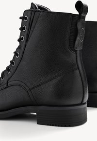 Botas de tobillo de cuero negro con acabado texturizado, puntera redondeada, diseño de cordones y suela de goma con tacón rectangular.