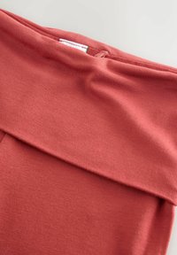 Material elastic și moale într-o nuanță corală discretă, cu un detaliu de talie pliată. Prezintă o textură netedă și o etichetă interioară cu instrucțiuni de întreținere.