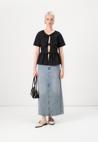 Svarte kortermede topp med knytning foran og peplumdesign, kombinert med en lys blå denimmaxiskjørt og beige slip-on sko, holder en svart veske.