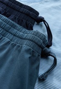 Deux paires de shorts à taille élastique bleus avec cordons de serrage posés sur une surface en tissu rayé bleu et blanc.