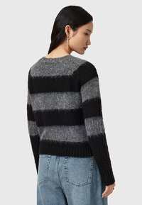 Maglione a righe nere e grigie con finitura testurizzata, scollo rotondo e orlo a coste. Indossato con jeans azzurri a vita alta.