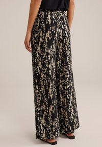 Pantalons larges en tissu noir avec un motif abstrait beige. Présentent une taille élastique et une texture lisse.