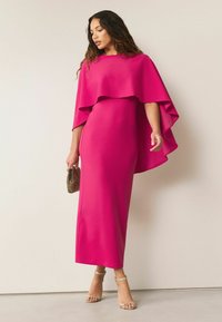 Fuksjowa sukienka z peleryną, dopasowana sylwetka i zwiewny dół. Połączona z sandałami na szpilkach i małą torebką z koralikami.