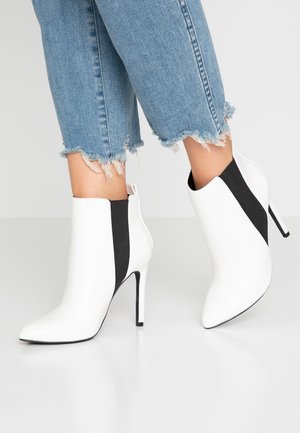 Bottines blanches à la conception épurée, pointues, avec de hauts talons aiguilles et des panneaux latéraux élastiques noirs. Finition avec une texture lisse.