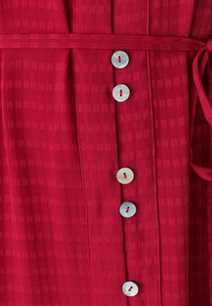 Rood patroon jurk met een textuurstof, vijf ronde, lichtgekleurde knopen langs de voorkant en een bijpassende ceintuur.