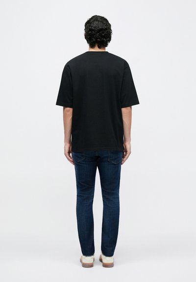 Melna īsroku T-krekls, standarta piegriezums, izgatavots no kokvilnas, ar apaļu apkakli. Valkāts kopā ar zilām džinsu biksēm un gaišas krāsas sporta apaviem.