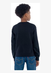 Svart sweatshirt laget av bomull, med klassisk rund hals og ribbede mansjetter, sammen med blå denimjeans som har et karakteristisk lomme-design.