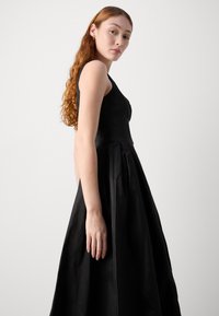 Black sleeveless dress with a fitted bodice and full, pleated skirt. Smooth texture, floor-length design, minimal embellishments and a simple silhouette.