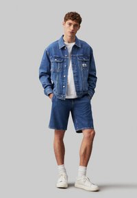 Denim jakk, millel on kaks rinna taskut, koos ühte moodi denim lühikeste pükstega. Kantud valge T-särgi peale ja kombineeritud valgete tossudega.