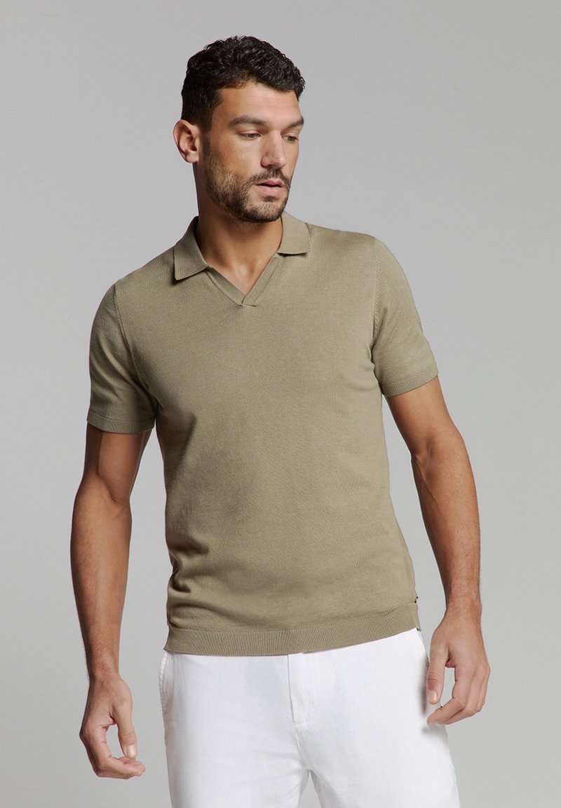 Korte mouw, V-hals pullover in olijfgroen gebreide stof, met een geribde zoom en manchetten. Gedragen met witte broeken.