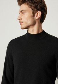 Schwarzer Pullover mit hohem Kragen, aus weichem Stoff gefertigt. Bietet eine figurnahe Silhouette und gerippte Details am Kragen und an den Bündchen.