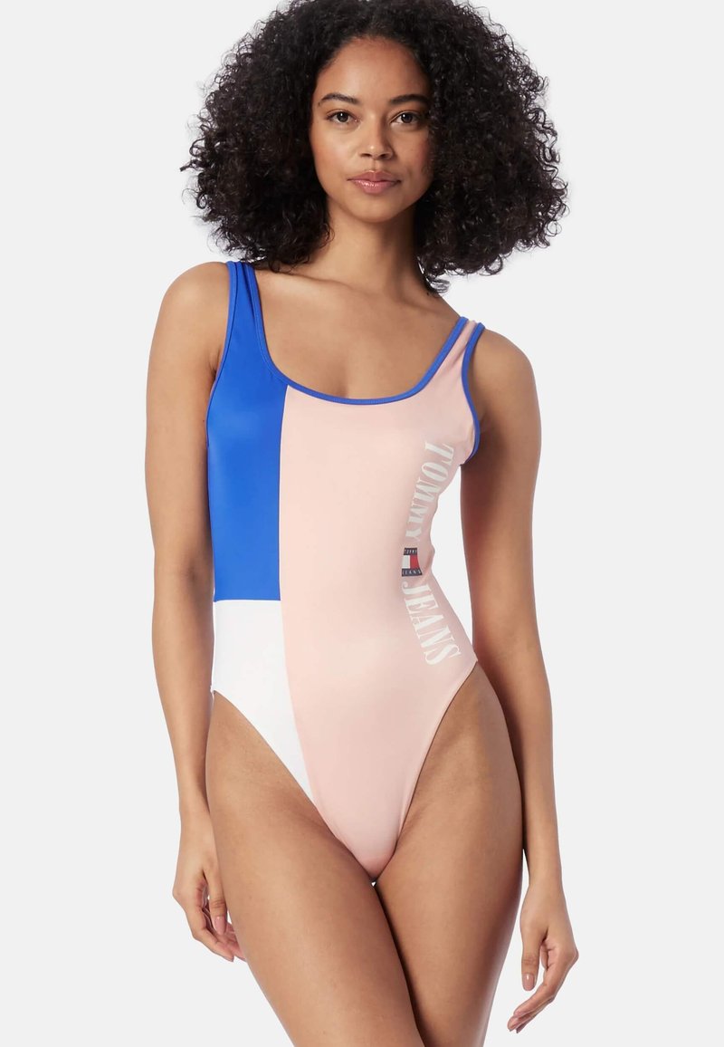 Bañador de una pieza colorido con paneles azules, rosas y blancos. Presenta un logo con el texto "TOMMY JEANS" en una fuente negrita en la parte delantera.