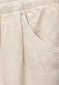 Tessuto di lino beige chiaro con una texture morbida, dotato di una tasca laterale e una vita arricciata con dettaglio a bottone.