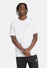 Biela krátka rukávová tričko s malým červeným logom na hrudi. Tkanina je hladká, s okrúhlym výstrihom a voľným strihom. Čierne nohavice s logom.