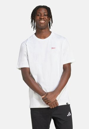 T-shirt bianco a maniche corte con un piccolo logo rosso sul petto. Il tessuto è liscio, con scollatura rotonda e vestibilità comoda. Pantaloni neri con logo.