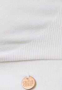 Tissu blanc à côtes avec une texture lisse, comportant une étiquette cousue avec une finition métallique cuivrée et un texte en relief.