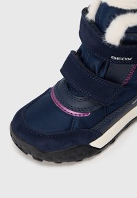 Tamsiai mėlyni žieminiai batai su Velcro diržais, rožinės spalvos detalėmis, tvirtu juodu padu ir baltu dirbtiniu pūku šalia kulkšnies.