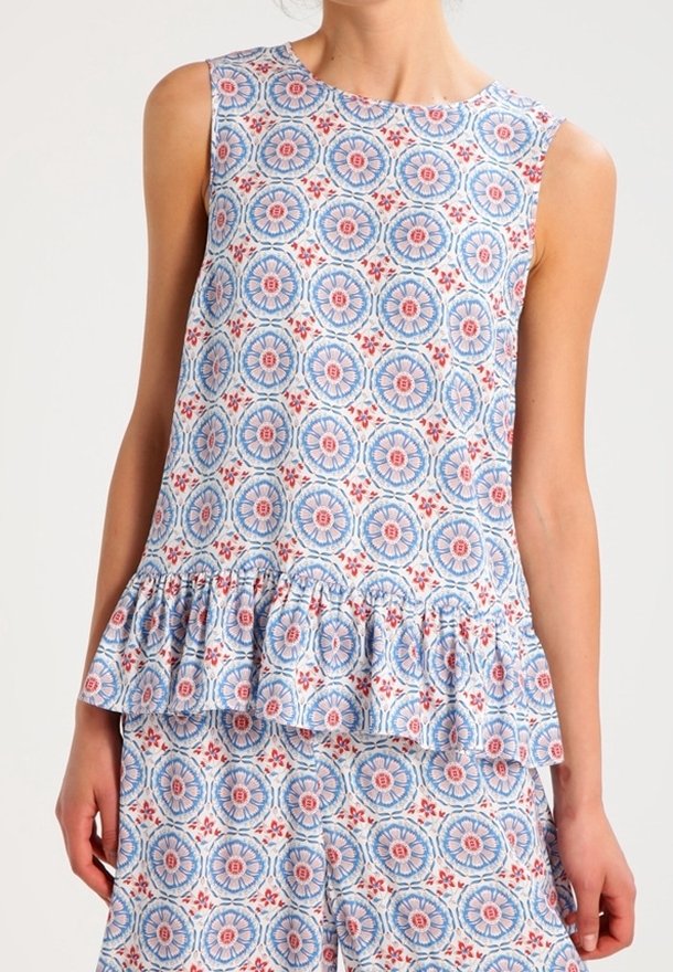 Top à imprimé floral en bleu, rouge et blanc avec un col rond, sans manches et un ourlet volanté. Présente des motifs circulaires sur l'ensemble.