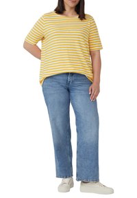 Gestreiftes gelbes und weißes T-Shirt mit lockerem Schnitt, kombiniert mit hellblauen weiten Jeans und weißen Sneakers. Kurze Ärmel und runder Ausschnitt.