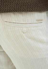 Fehér csíkos nadrág, könnyű textúrával, hátsó zsebbel, gombos záródással és "JACK & JONES" feliratú márkajeggyel.