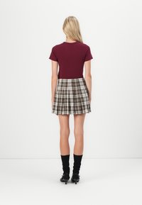 Burgundy short-sleeve top paired with a pleated plaid skirt featuring beige, brown, and green tones. Black knee-high socks and heels complete the look.