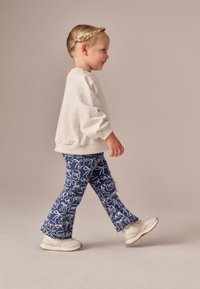 Felpa grigio chiaro con maniche a sbuffo, abbinata a pantaloni blu a zampa con motivi illustrati bianchi, completata da sneakers bianche.