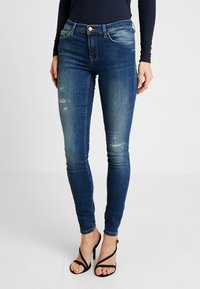 Kapeat siniset farkut, joissa haalistunut pesu ja liev�ää kulutusta, viisi taskua ja metallinen nappisuljin. Yhdistetty mustiin korkokenkiin.