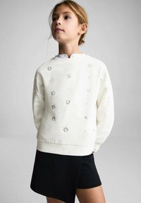 Vit sweatshirt med blommor och texturerade prickar, matchad med svarta shorts. Har rund hals och avslappnad passform.