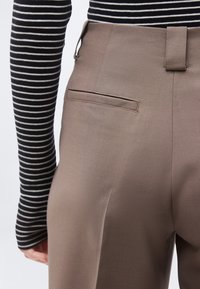 Κοντινό πλάνο ατόμου που φοράει καφέ γκρι παντελόνι ταιριαστού σχεδίου και μακρυμάνικο τοπ με μαύρες και λευκές ρίγες, εμφανίζοντας τη λεπτομέρεια της πίσω τσέπης.