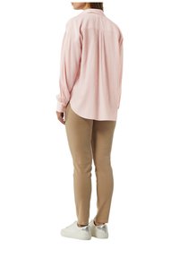 Lichtroze langesleeve shirt met verticale ribbels, gecombineerd met beige slim-fit broek en witte sneakers met zilveren accenten.