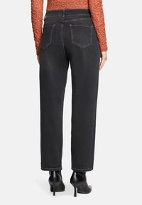 Jean noir taille haute avec une coupe décontractée, dotés de deux poches arrière et de coutures contrastées, associés à des chaussures à talons noires.