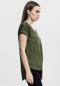T-shirt verde oliva a maniche corte con una vestibilità ampia, scollo rotondo e orlo posteriore più lungo, realizzato in un morbido tessuto testurizzato.